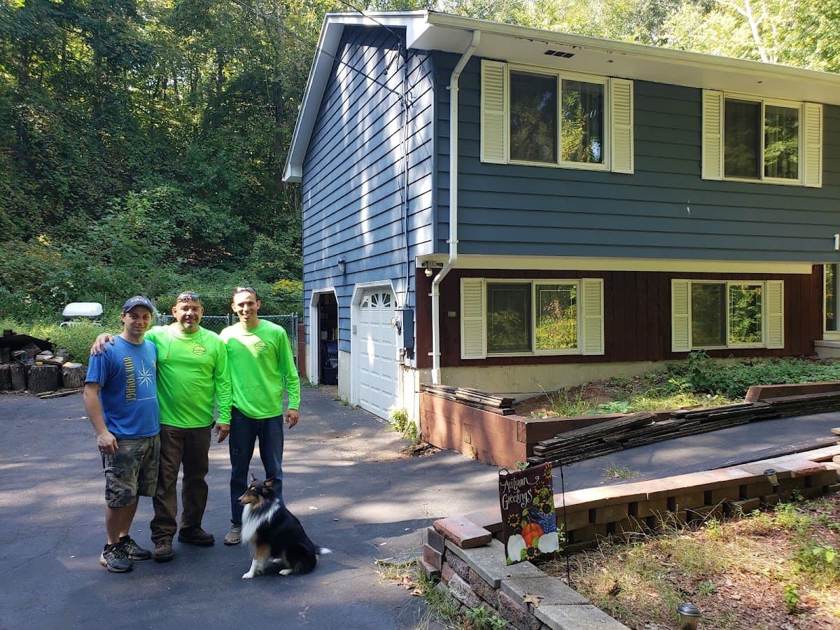 Three crew members and a dog standing in a driveway in front of a blue house.